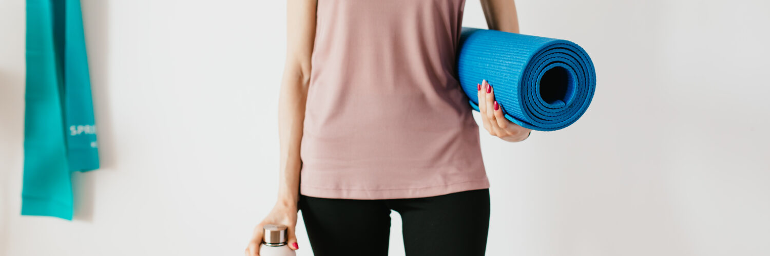 Crop sportswoman carrying sport mat and bottle of water before exercising