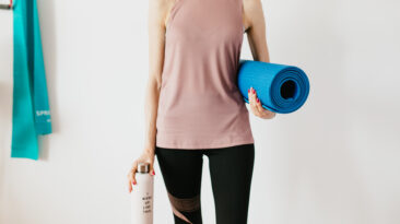 Crop sportswoman carrying sport mat and bottle of water before exercising
